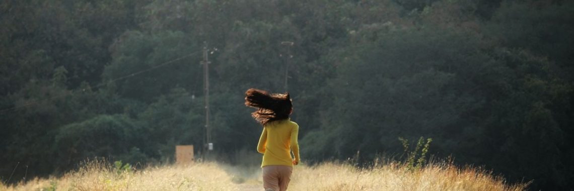 Young woman with long hair runs down a scenic path in summer. Embracing freedom and nature.